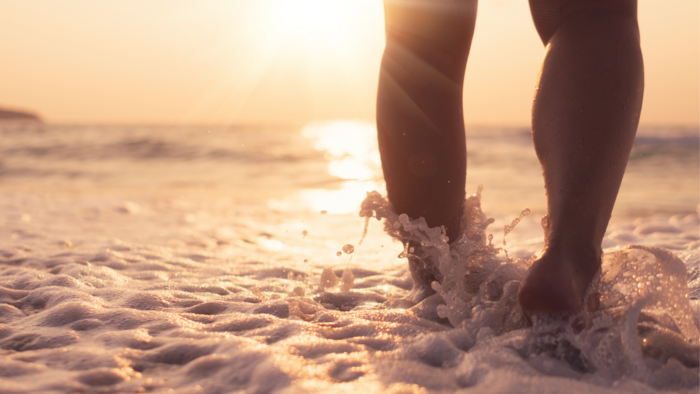 Füße die durch Meeresschaum am Strand laufen. 