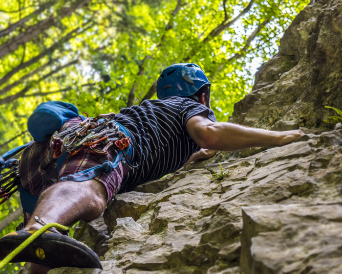 Ein Mann klettert an einem Felsen hoch, gesichert durch ein Kletterseil.